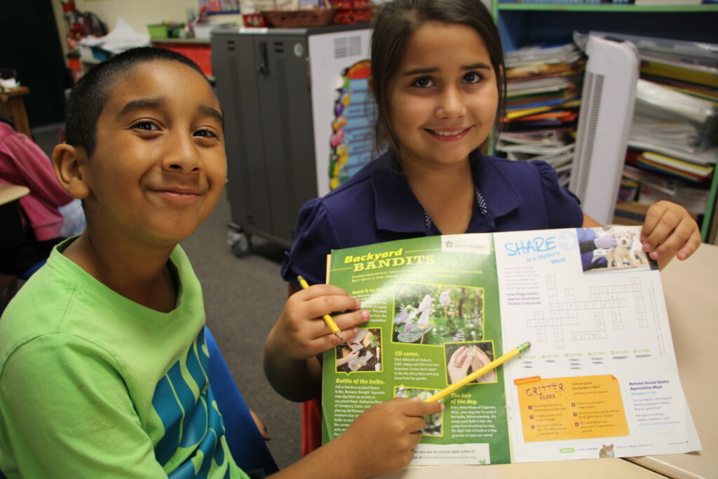 Two students holding Kind News magazine and smiling