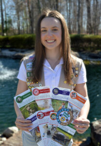 A girl with long brown hair in a Girl Scouts uniform holds animal safety pamphlets and smiles.